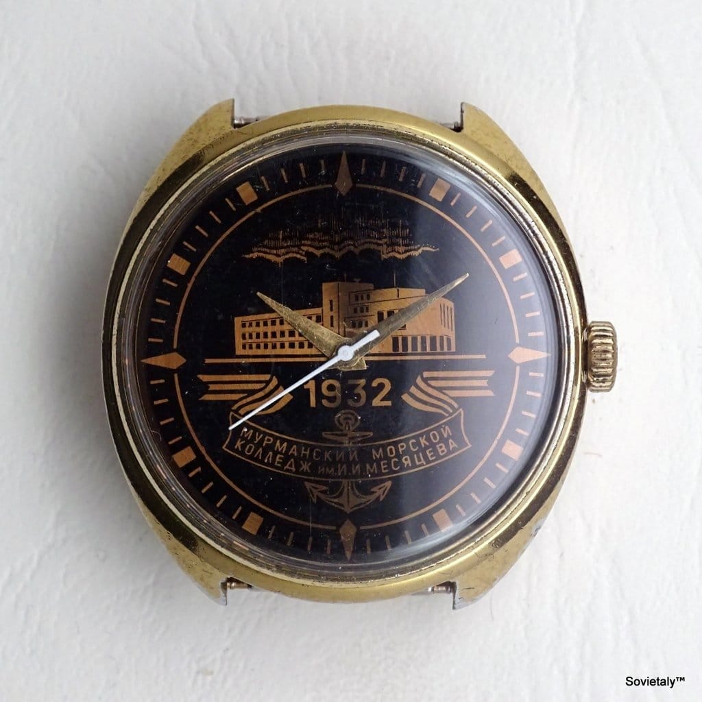 Primo piano di un orologio con quadrante nero e dettagli dorati, recante la scritta in cirillico "1932" e "МУРМАНСКИЙ МОРСКОЙ КОЛЛЕДЖ ИМ. И. МЕСЯЦЕВА". Proprietà di Sovietaly.