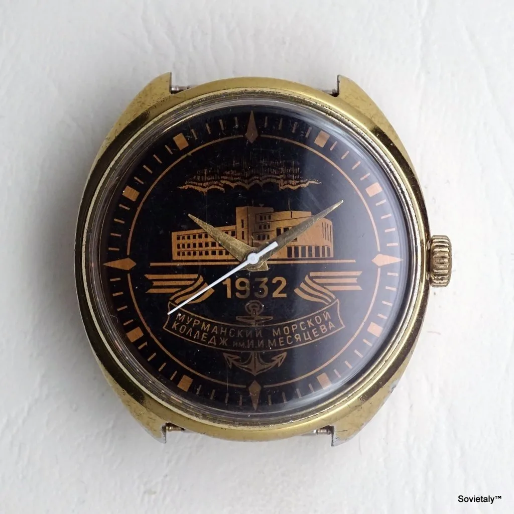 Primo piano di un orologio con quadrante nero e dettagli dorati, recante la scritta in cirillico "1932" e "МУРМАНСКИЙ МОРСКОЙ КОЛЛЕДЖ ИМ. И. МЕСЯЦЕВА". Proprietà di Sovietaly.